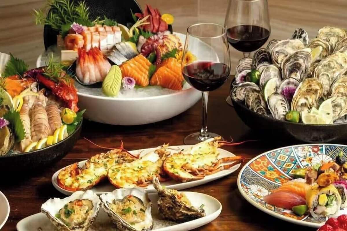 A variety of seafood dishes, including oysters, shrimp, and sushi, arranged on a wooden table.