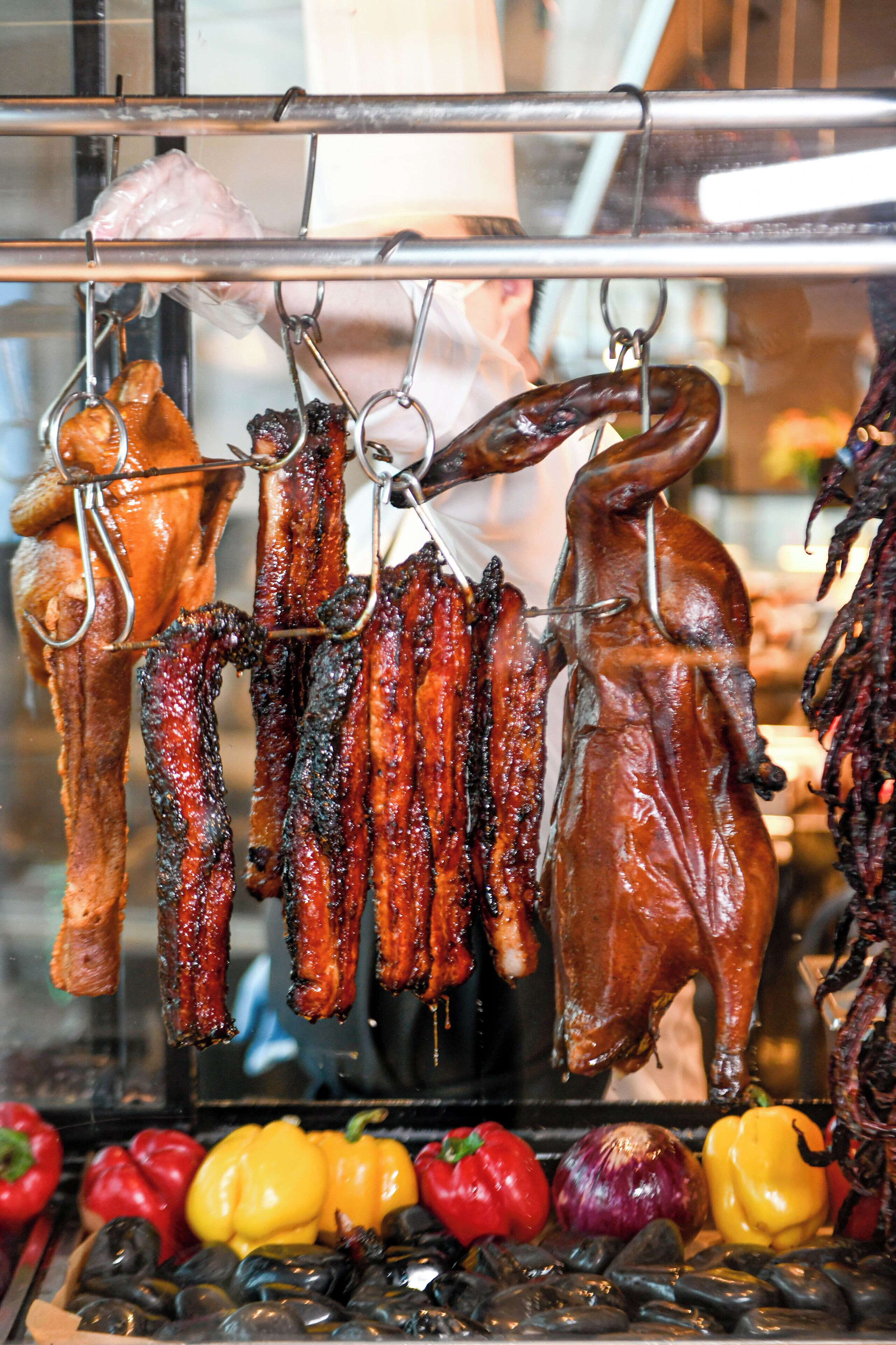 Variedad de carnes colgadas en ganchos, incluyendo salchichas y un cerdo asado entero.