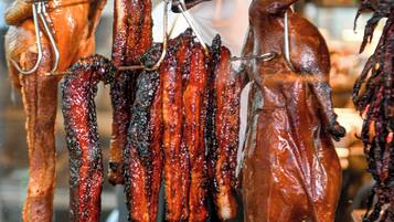 Variedad de carnes colgadas en ganchos, incluyendo salchichas y un cerdo asado entero.