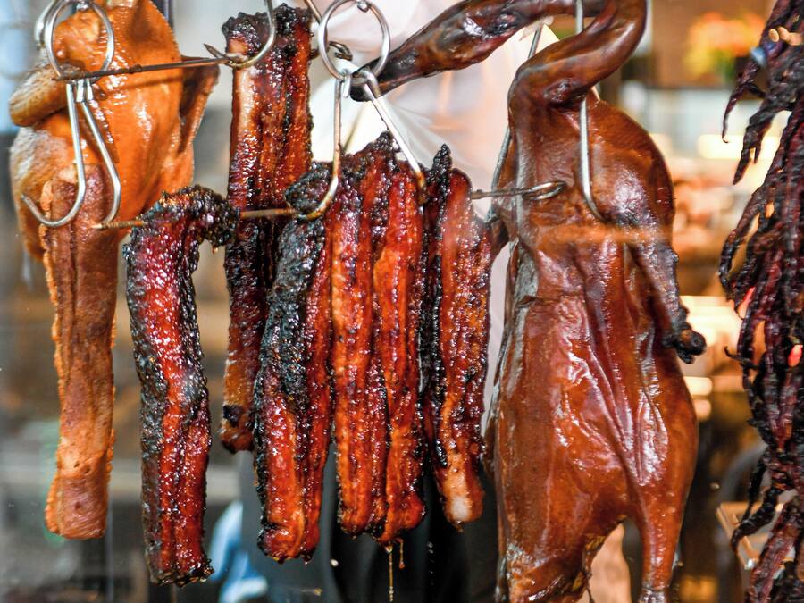 Variedad de carnes colgadas en ganchos, incluyendo salchichas y un cerdo asado entero.