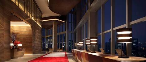 A modern hotel lobby with a red carpet, large windows, and contemporary lighting fixtures.
