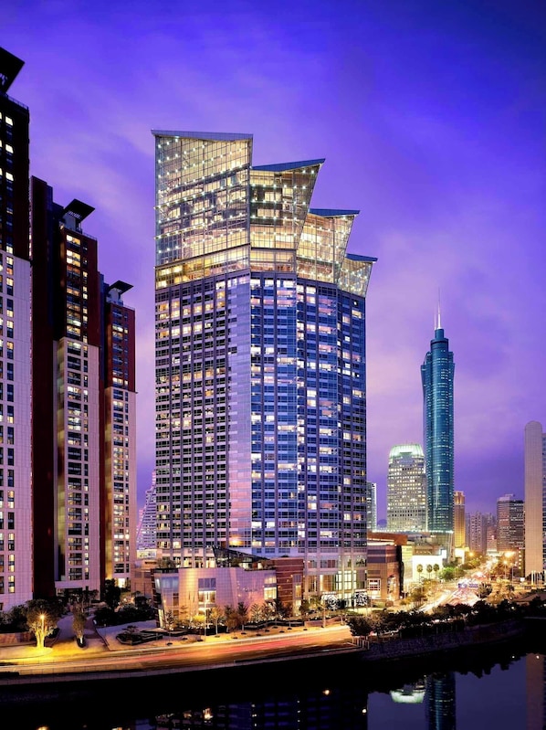 A modern high-rise building with a unique angular design, surrounded by other tall buildings and a body of water.