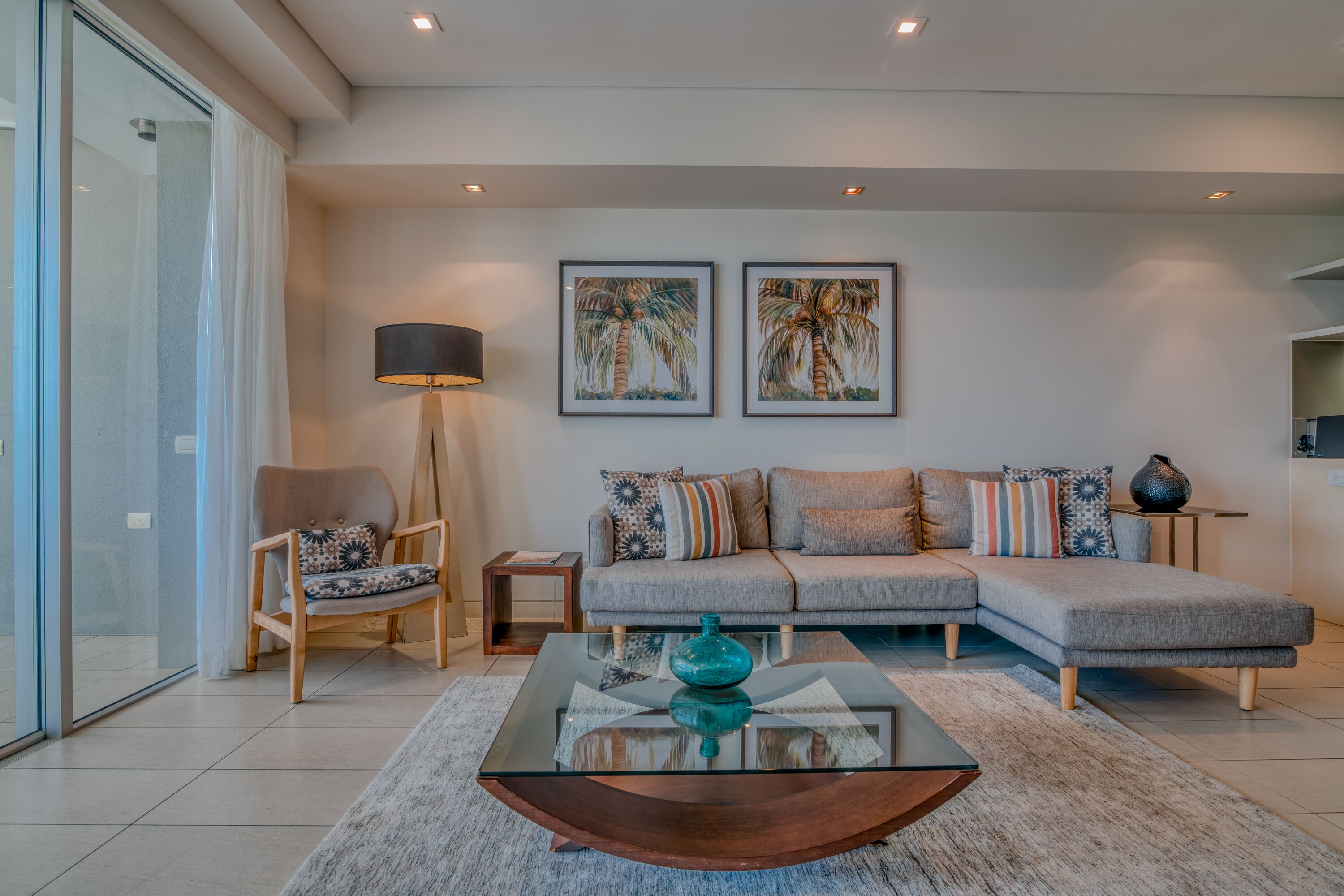 Una sala de estar moderna con un sofá modular, una mesa de centro de vidrio y dos obras de arte enmarcadas en la pared.