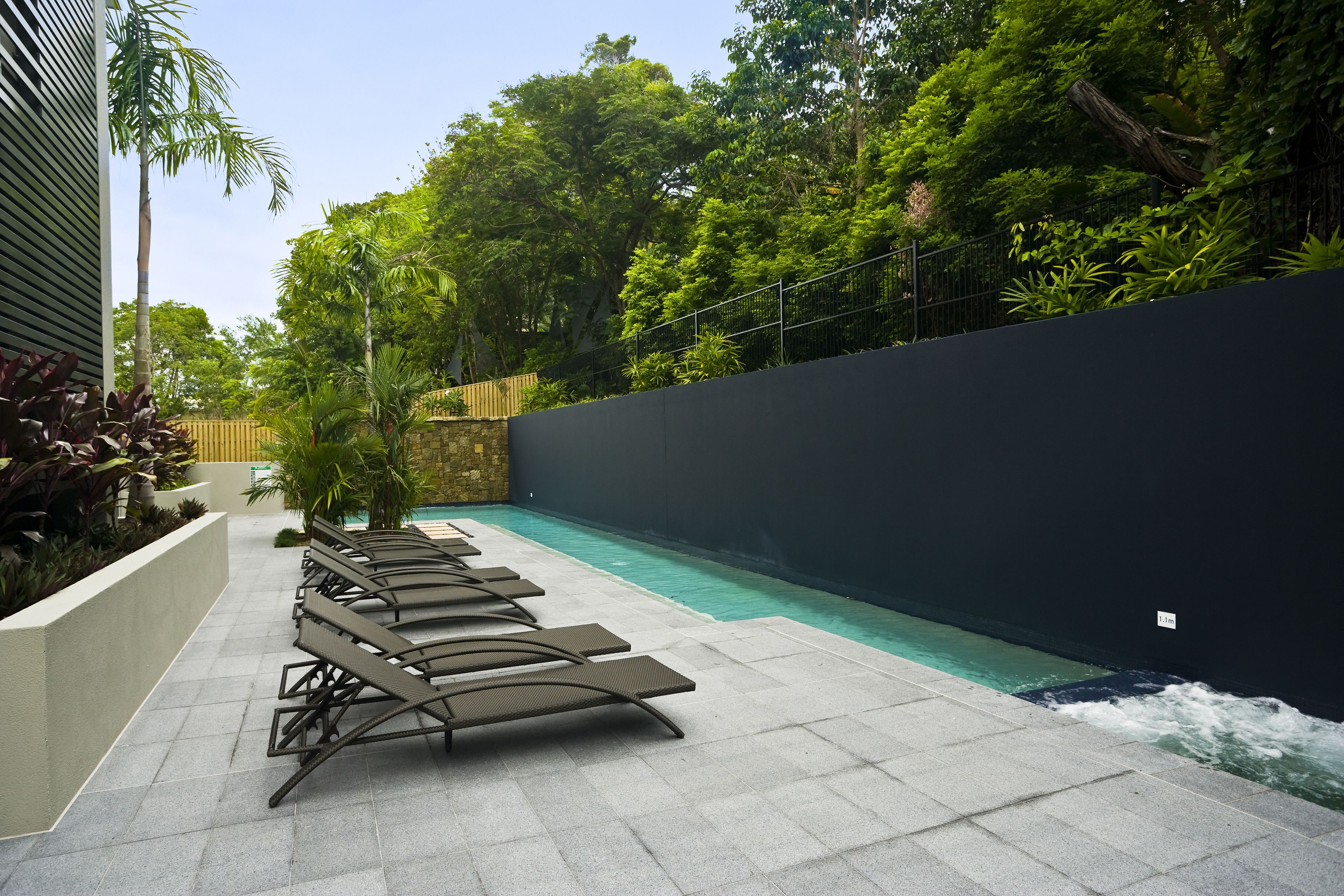 A poolside area with lounge chairs, a stone wall, and lush greenery.