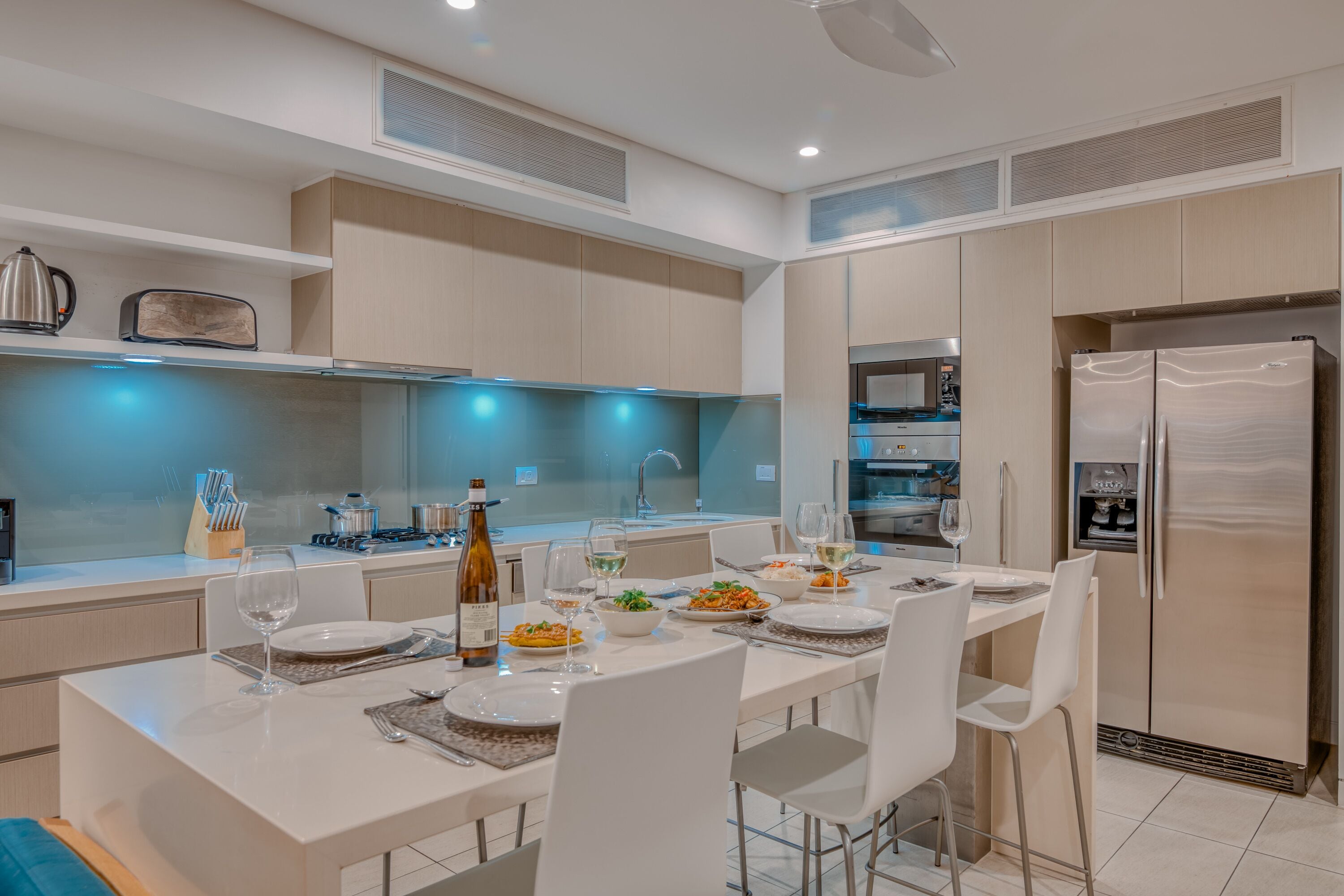 A modern kitchen with white cabinetry, a stainless steel refrigerator, and a dining table set for four.