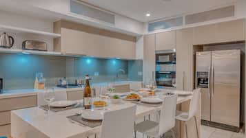 A modern kitchen with white cabinetry, a stainless steel refrigerator, and a dining table set for four.