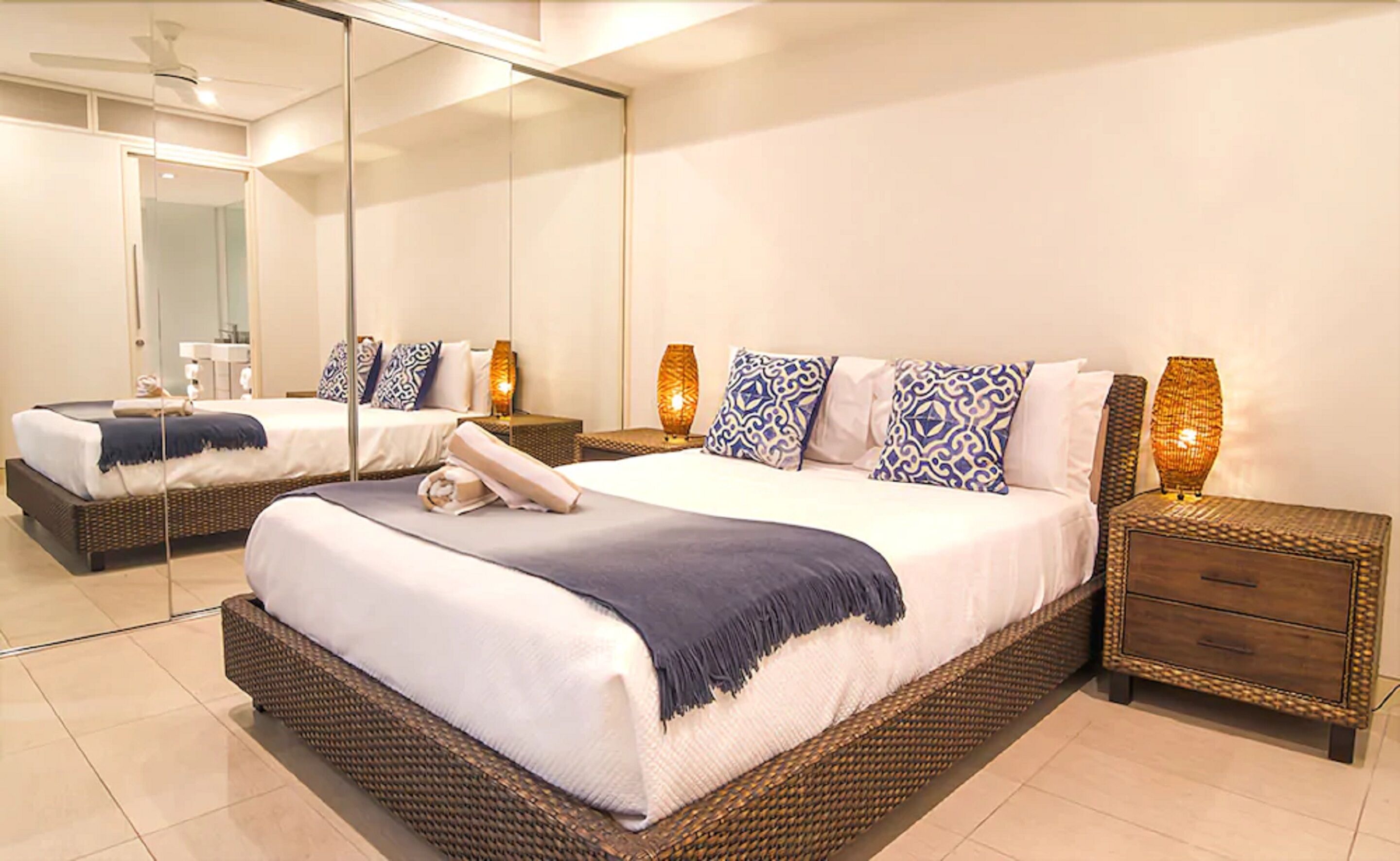 Habitación de hotel moderna con una cama grande, dos mesitas de noche, un espejo y un baño visible a través de la puerta de cristal.
