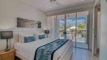 A modern bedroom with a large bed, a ceiling fan, and a view of the outdoor balcony.
