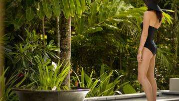 A woman in a swimsuit standing by a pool with lush greenery in the background.