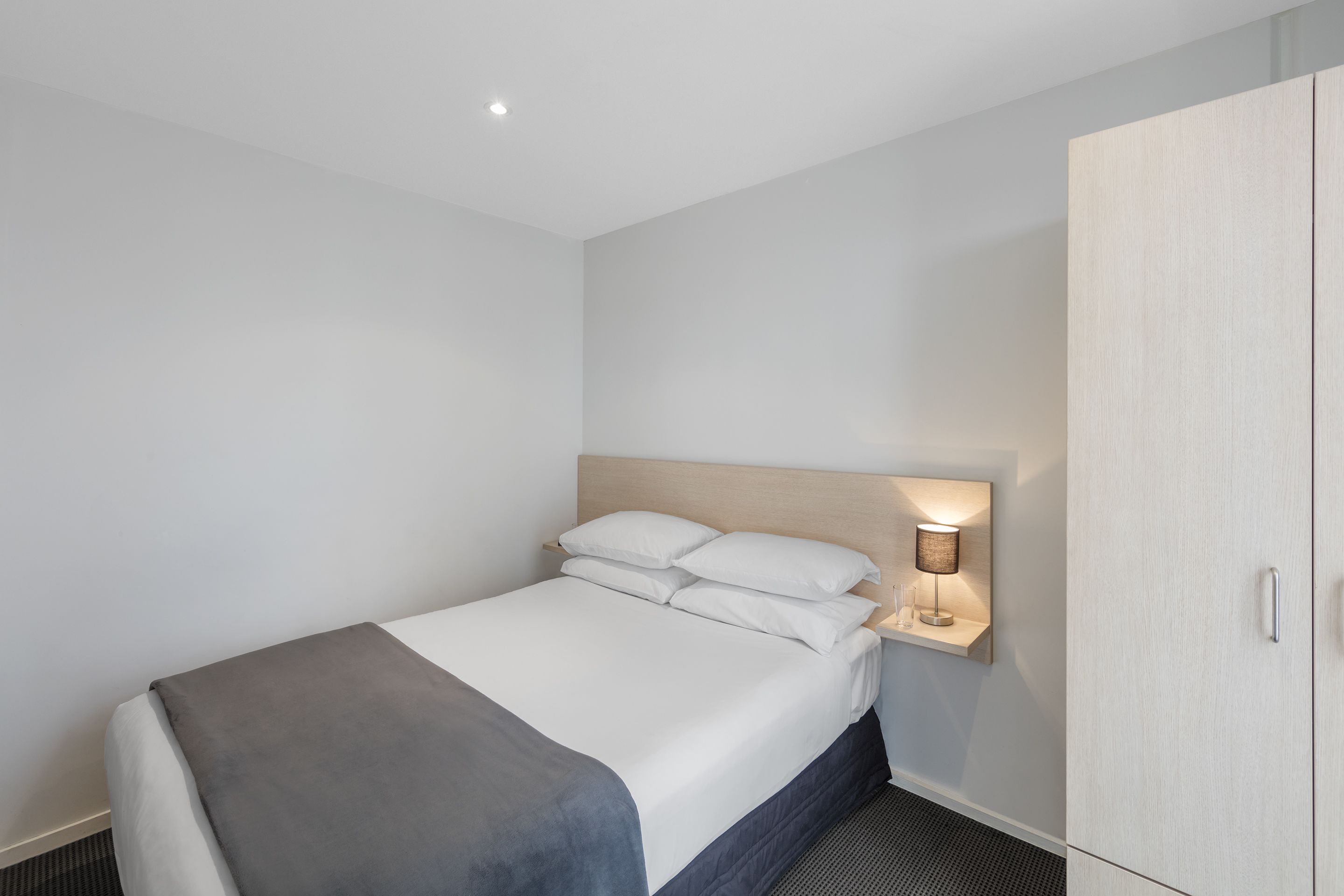 A hotel room with a bed, a bedside table with a lamp, and a wardrobe.