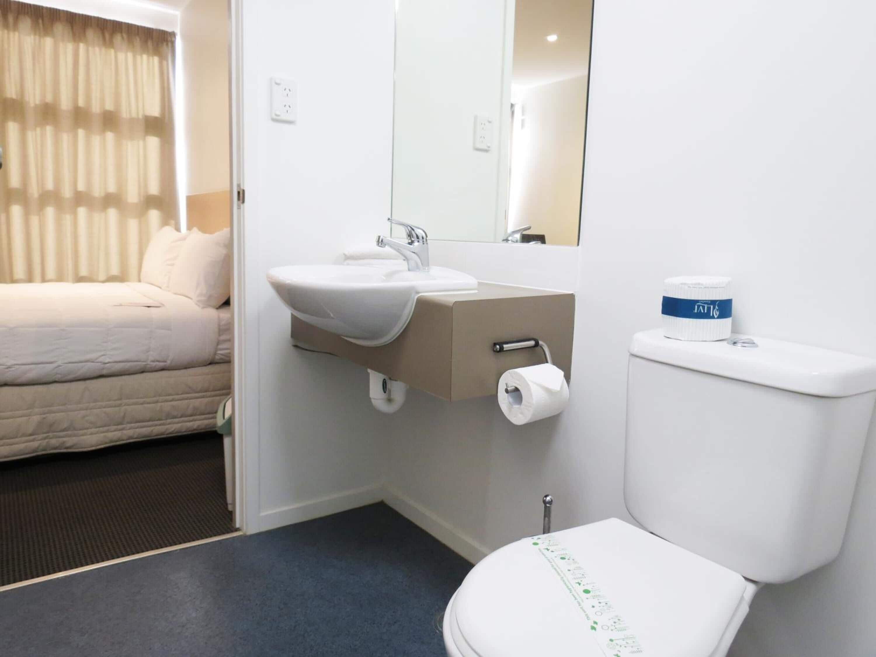 Un baño de hotel con cama, lavamanos, inodoro y espejo.