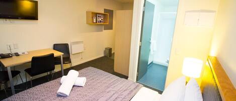 A hotel room with a bed, a desk, a chair, a television, and a door leading to a bathroom.