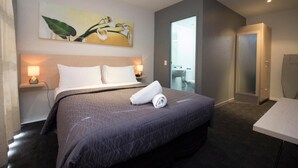A hotel room with a large bed, a bedside table with a lamp, a painting on the wall, and a door leading to a balcony.