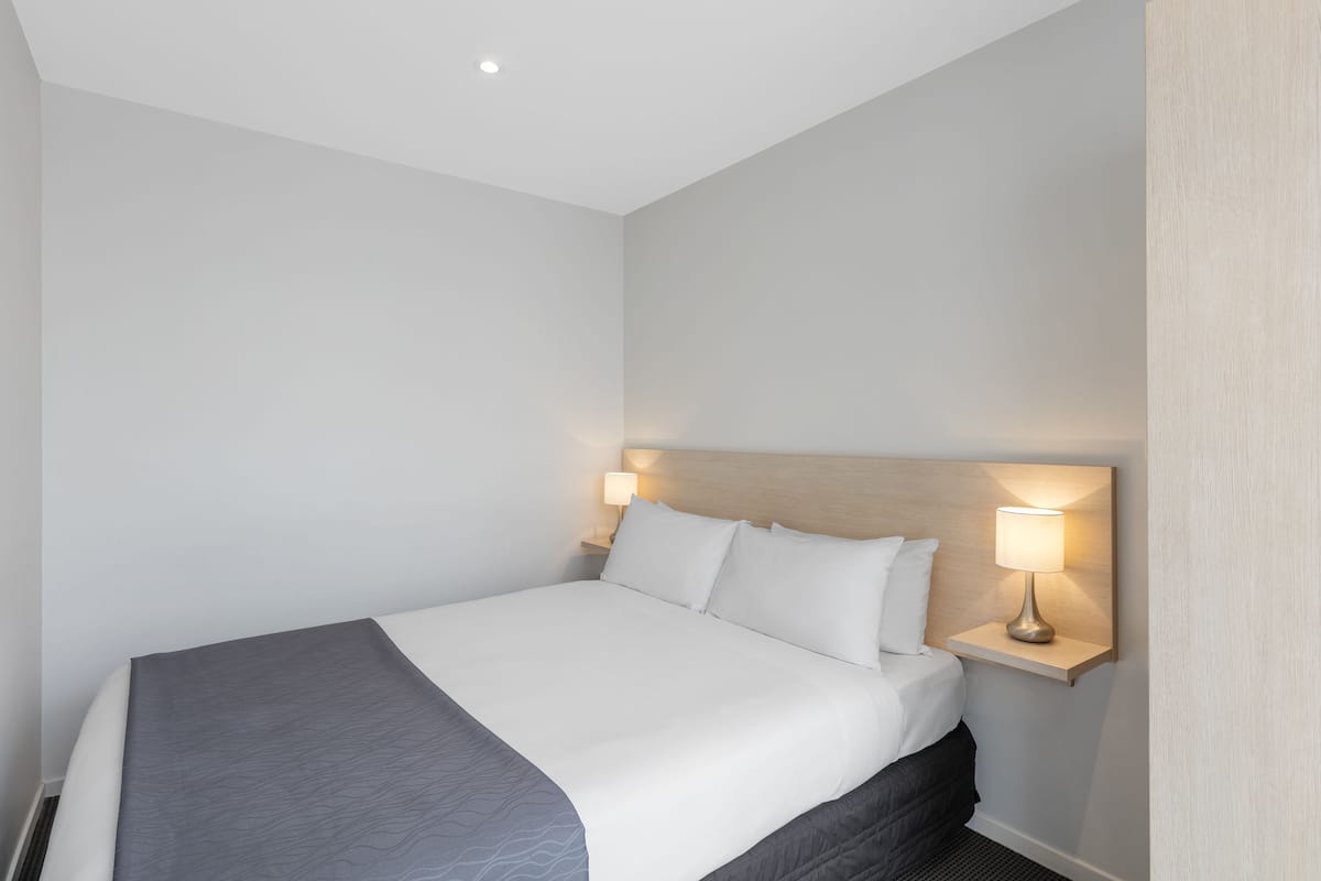 A neatly made bed with white linens and a grey throw blanket, flanked by two bedside lamps on a wooden nightstand.