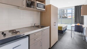 A compact kitchenette with a microwave, sink, and stove. There is a small dining area with a table and chairs.