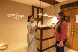 A reception area with a wooden reception desk, a neon sign reading "the ayur gunga spa", and a large mirror above the desk.