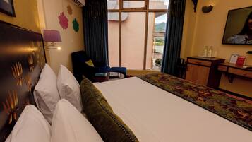 A hotel room with a large bed, a desk with a chair, a window with curtains, and a wall-mounted TV.