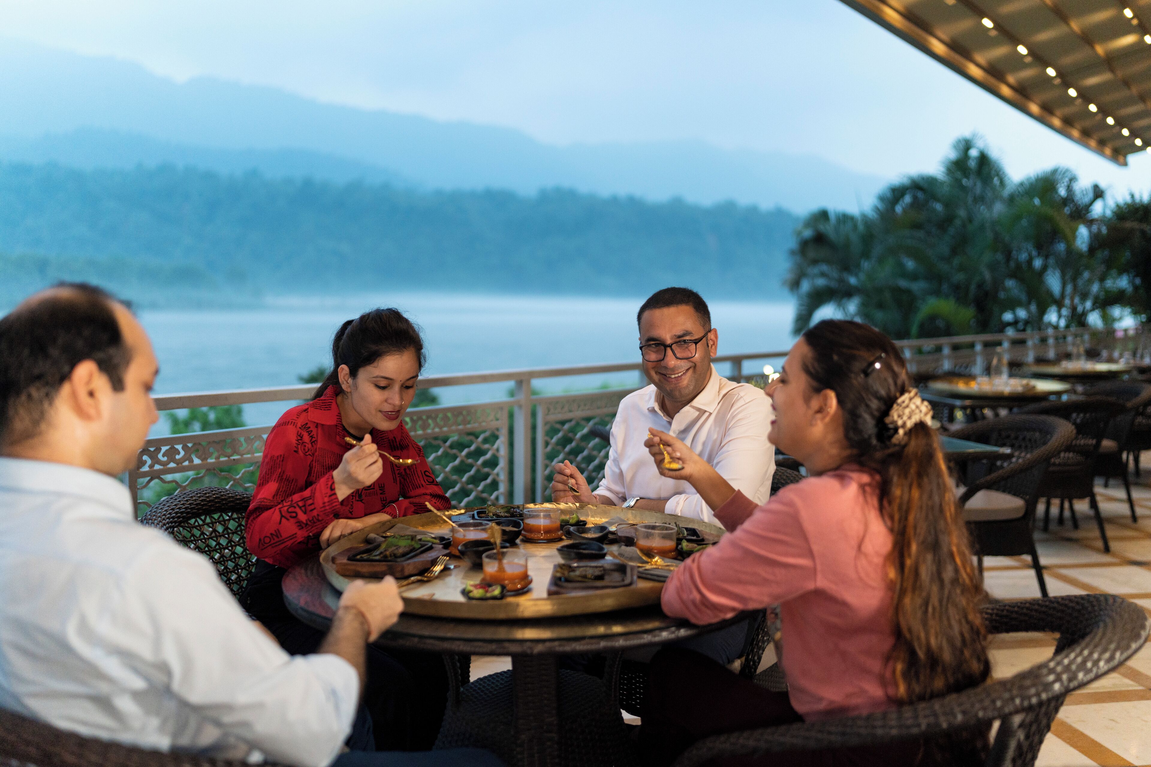 A group of people dining at an outdoor table with a scenic view of mountains and a body of water.