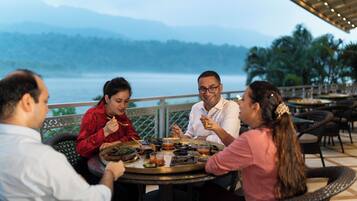 A group of people dining at an outdoor table with a scenic view of mountains and a body of water.