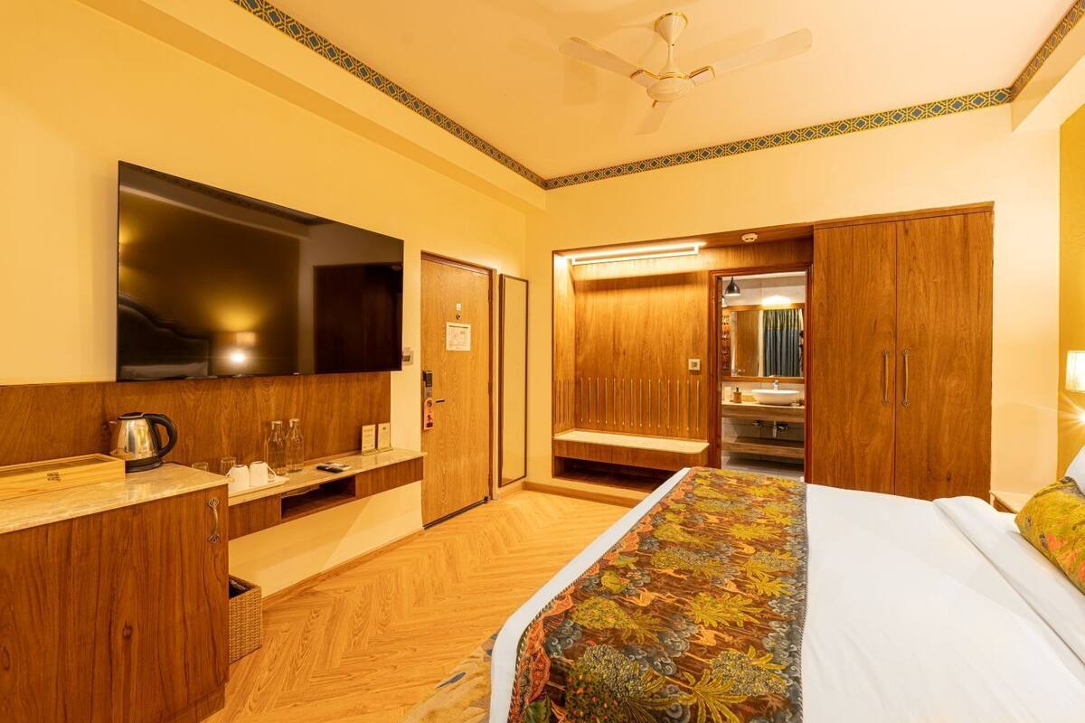 Una habitación de hotel con una cama, televisión, armario de madera, baño con espejo y ventilador de techo.