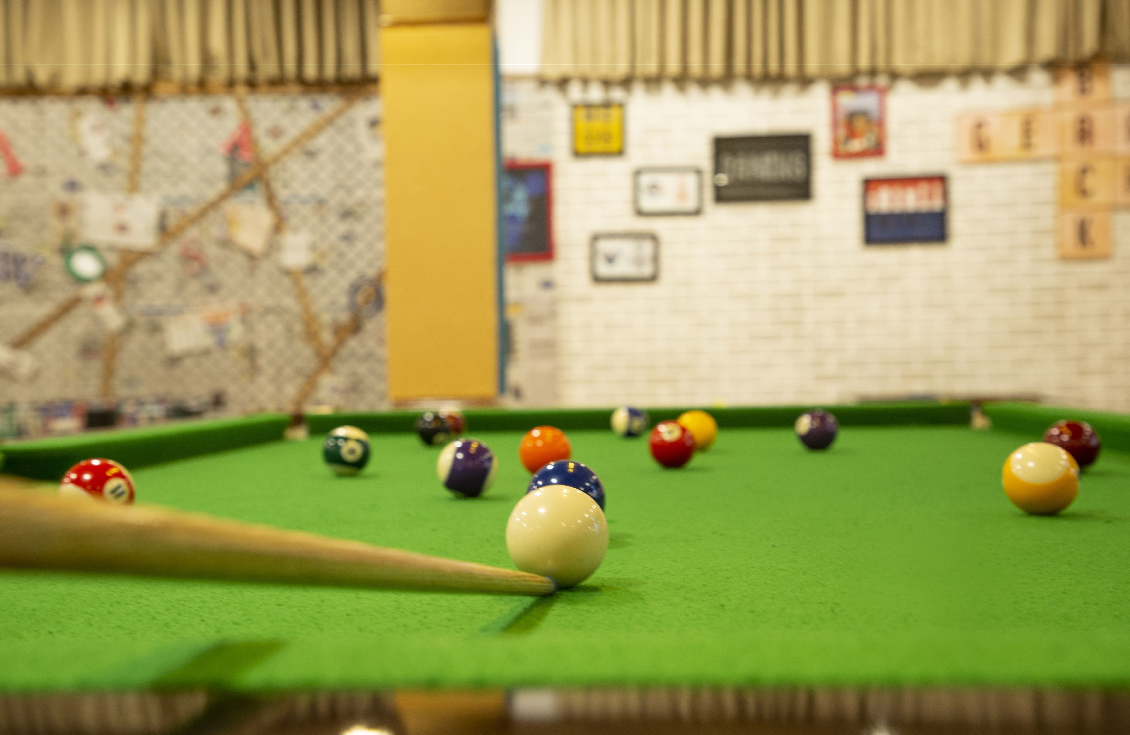 A pool table with balls and a cue stick, a brick wall with various signs, and a map on the wall.