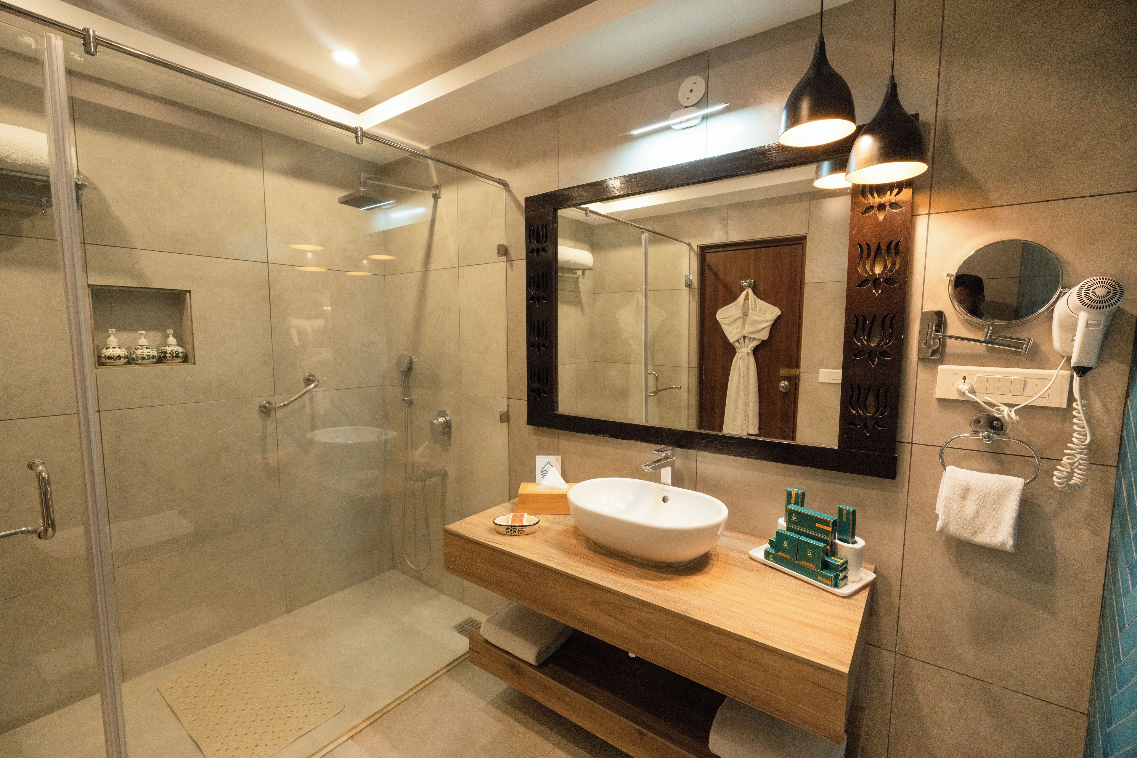 A modern bathroom with a glass shower enclosure, a wooden vanity with a large mirror, and a hairdryer mounted on the wall.