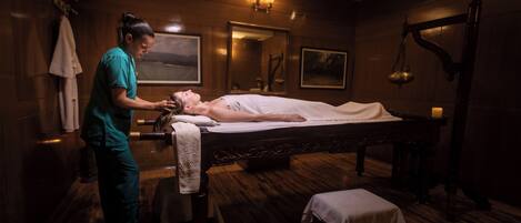 Une salle de massage dotée d’un plancher en bois, d’une table de massage, d’une serviette, d’une balance et d’un miroir.
