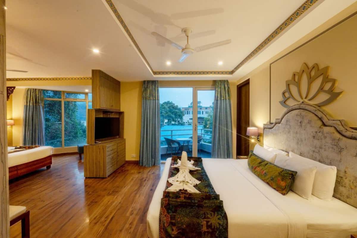 Habitación de hotel con una cama grande, televisor, balcón con vistas y ventilador de techo.