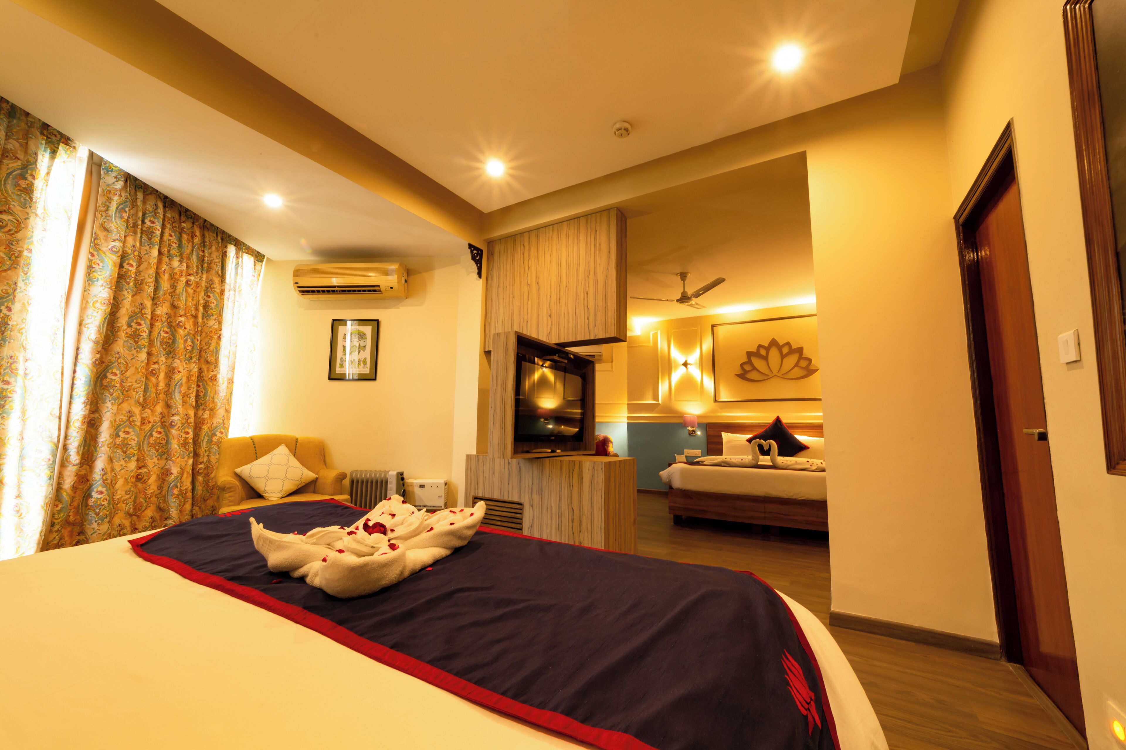 Habitación de hotel con una cama grande, zona de estar con una silla y una mesa, baño con ducha y vistas al pasillo.