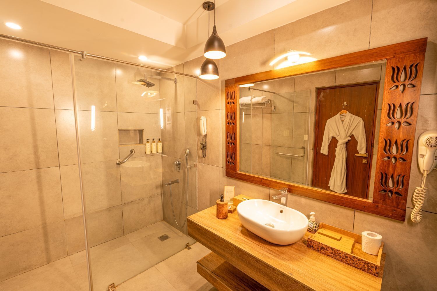 A modern bathroom with a glass-enclosed shower, a wooden vanity with a sink, a large mirror, and a hairdryer on the wall.