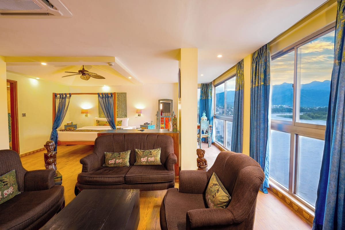 Habitación de hotel con una cama grande, un sofá, una mesa de centro y vistas a la montaña desde la ventana.