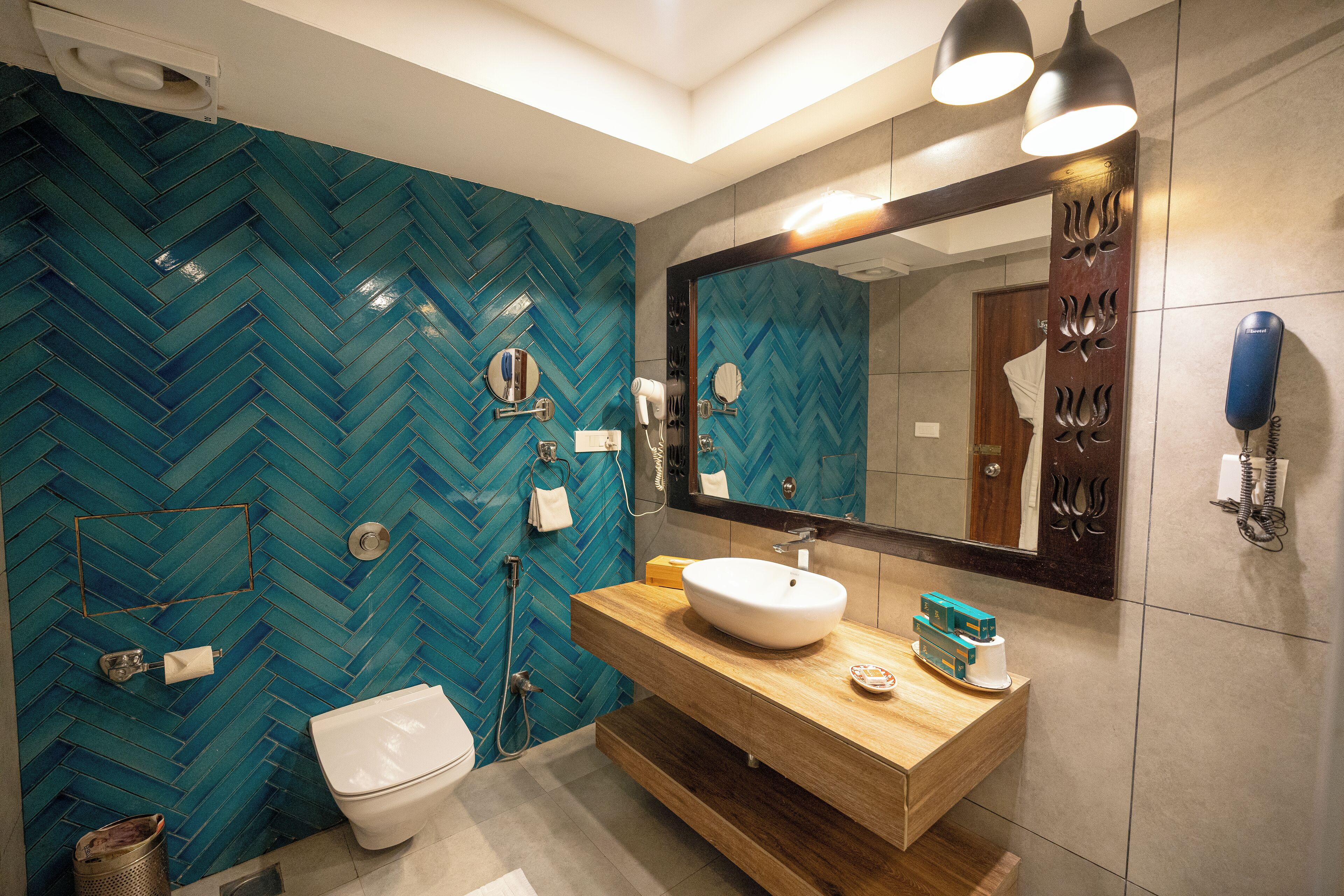 Un baño moderno con patrón de baldosas en espiga, tocador de madera, lavamanos blanco y espejo con teléfono.