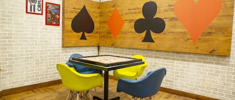 Une pièce avec un baby-foot, des chaises colorées et un mur orné de grands motifs représentant des symboles de cartes à jouer.