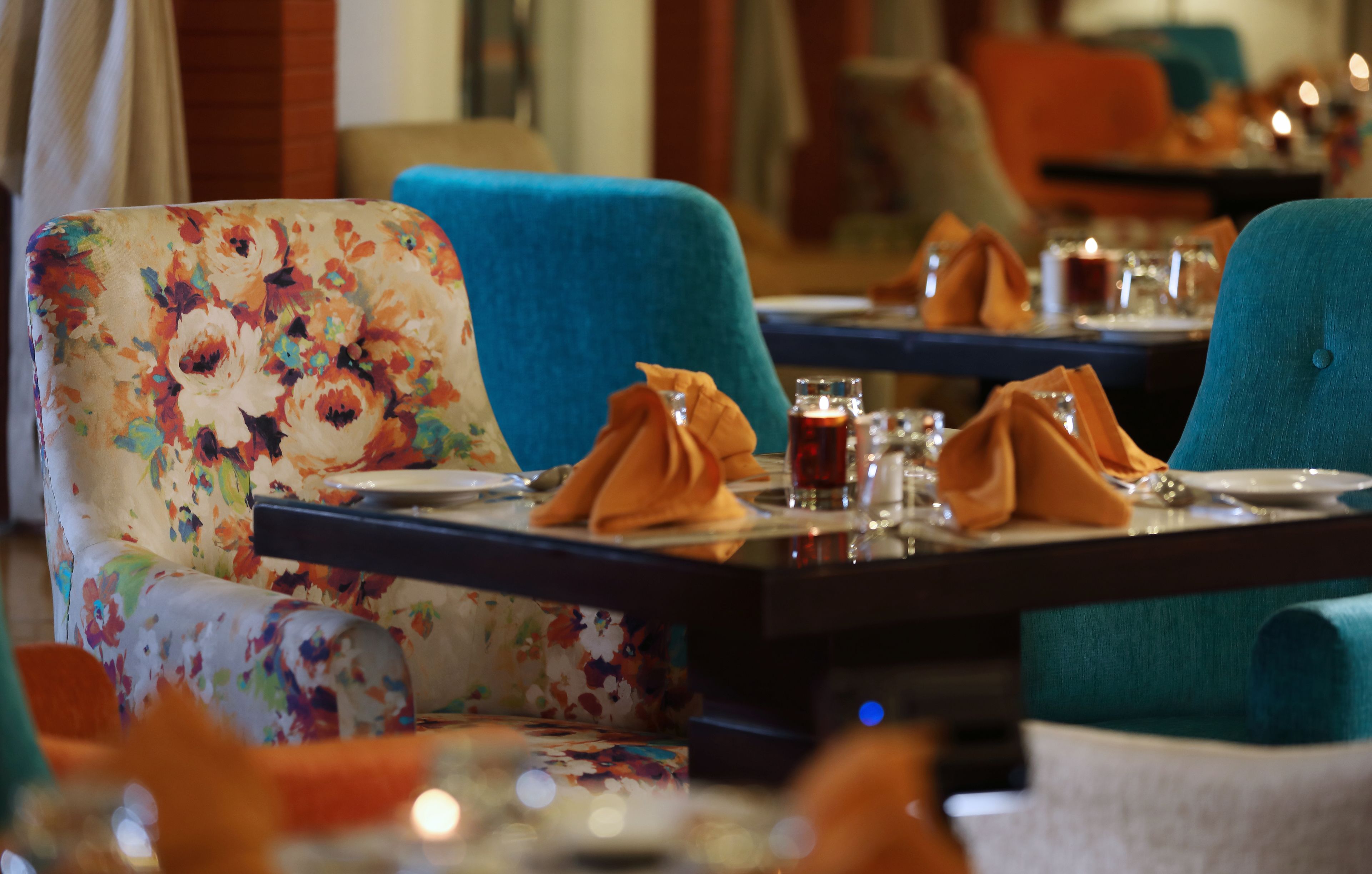 Un ristorante con sedie a motivi floreali, tovaglioli arancioni e tavoli illuminati da candele.