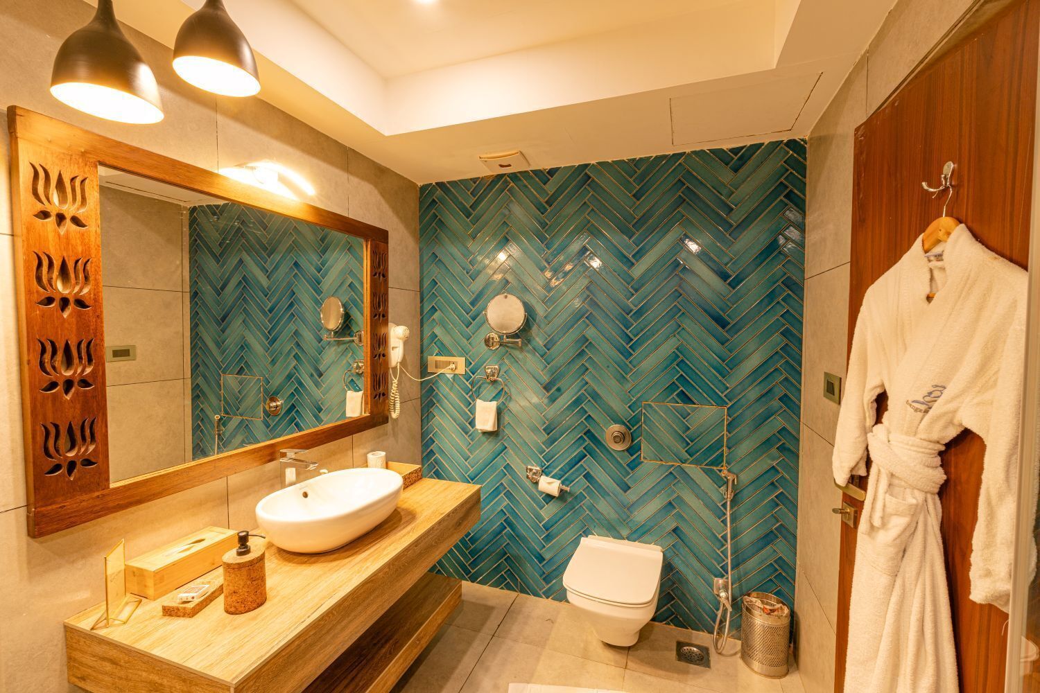 A modern bathroom with a herringbone tile backsplash, a wooden vanity with a sink, a mirror, and a robe hanging on the door.