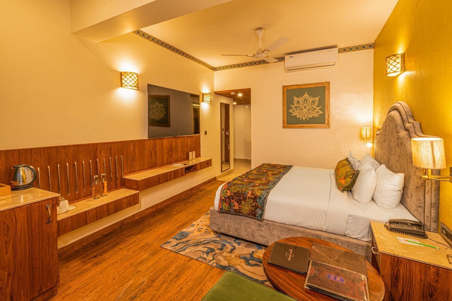 A hotel room with a bed, bedside table, lamp, and a desk with a chair.