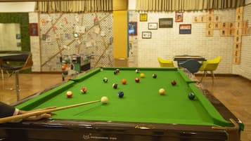A pool table with balls, a pool cue, and a table tennis table in a room with a brick wall and a green wall with a map.