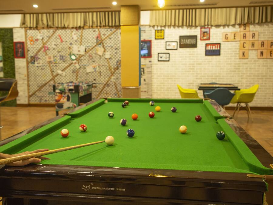 A pool table with balls, a pool cue, and a table tennis table in a room with a brick wall and a green wall with a map.