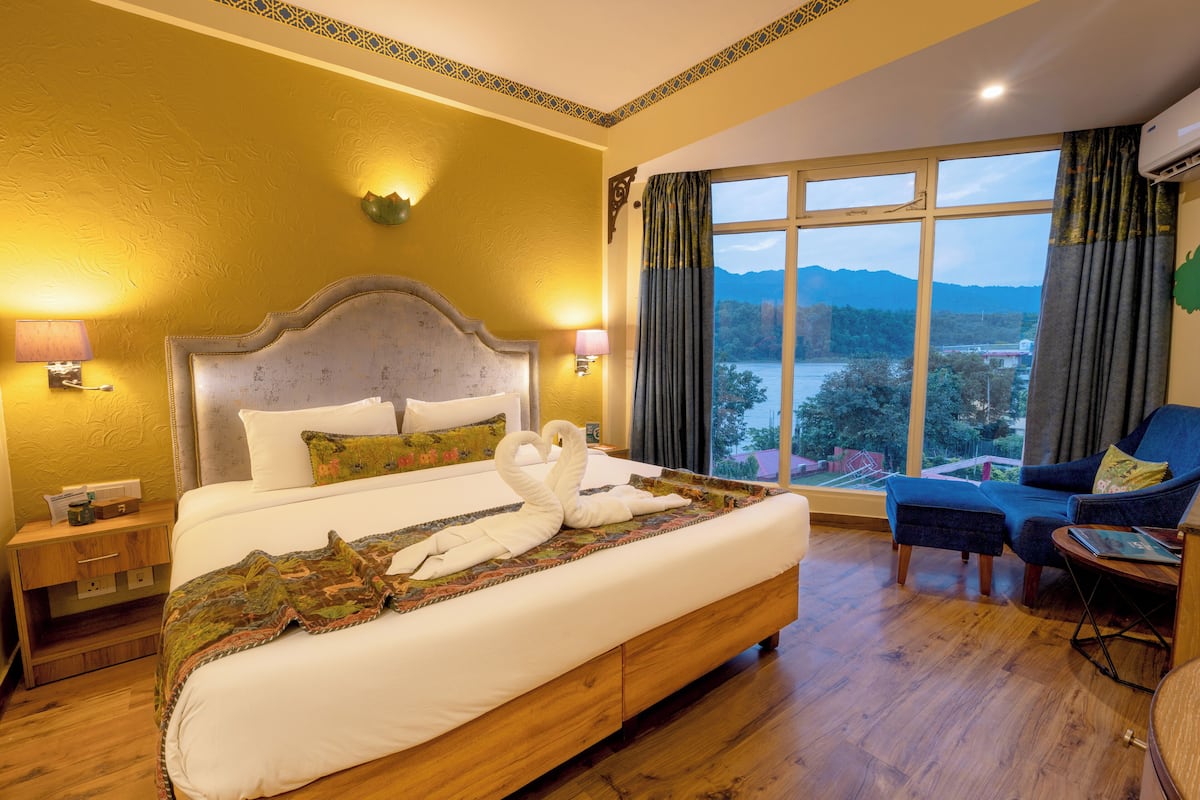 Habitación de hotel con una cama grande, vistas a las montañas y un rincón de descanso con una silla y un reposapiés azules.