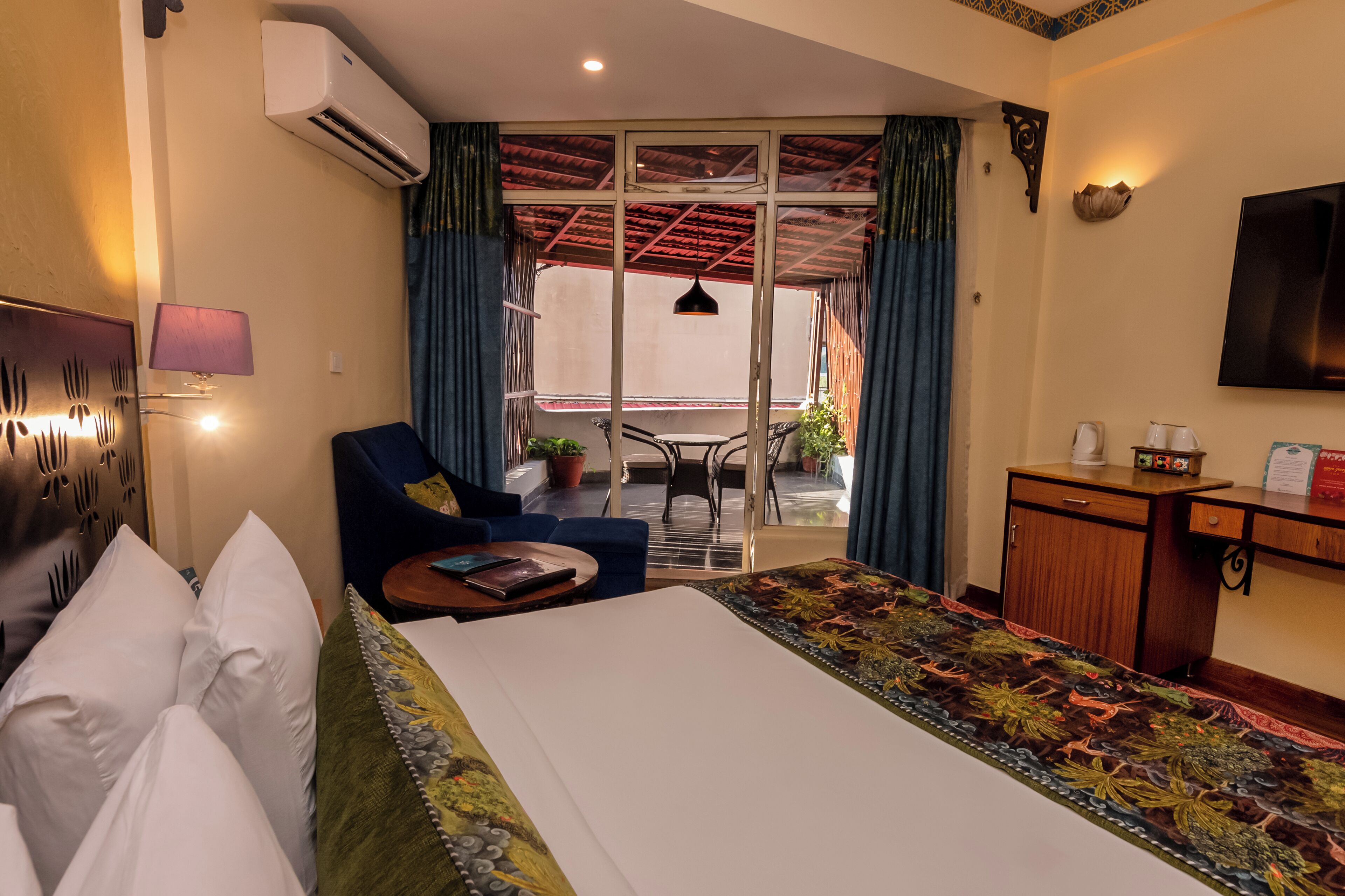 A hotel room with a bed, a desk, a chair, a small table, a lamp, and a television.