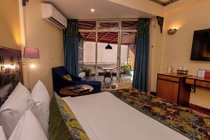 A hotel room with a bed, a desk, a chair, a small table, a lamp, and a television.