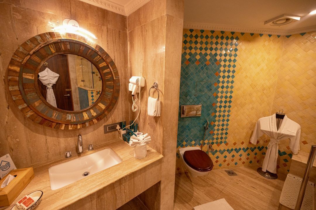 Un baño con un espejo grande, lavamanos e inodoro. Hay un perchero y una bata colgada en la pared.