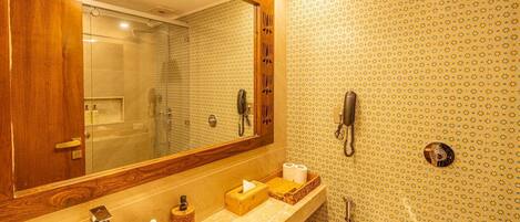 A bathroom with a large mirror, a sink, a toilet, and a shower. There are two phones mounted on the wall.