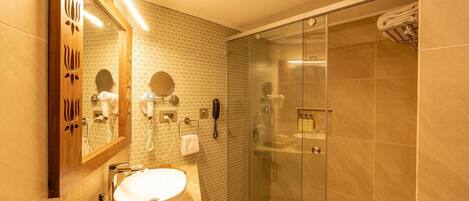 A modern bathroom with a large sink, a mirror, a hairdryer, a telephone, and a glass-enclosed shower area.