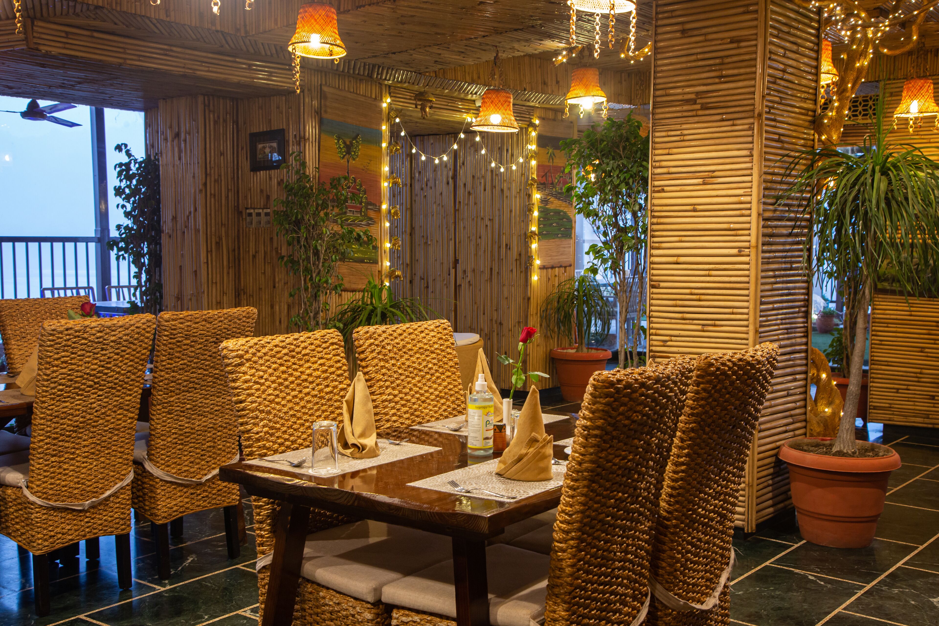 Un restaurant avec des meubles en osier, des tables avec des serviettes et des plantes en pot.