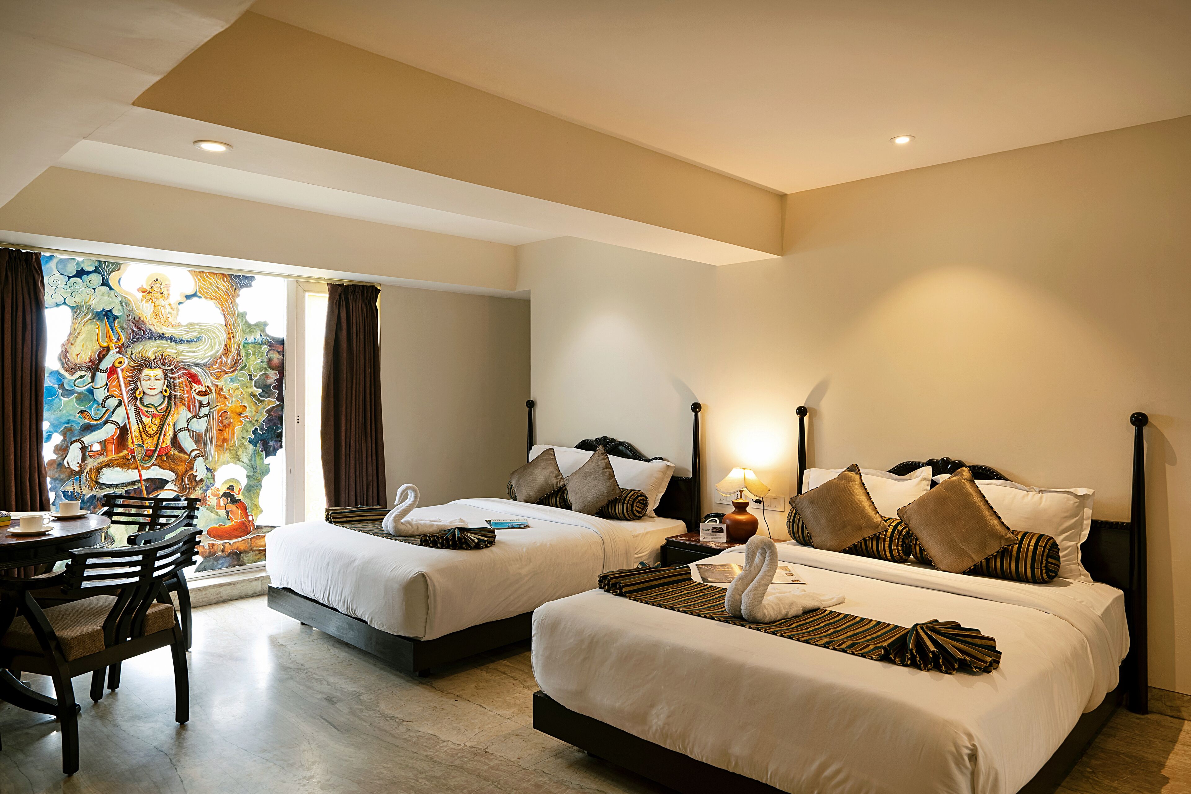 A hotel room with two beds, a dining table, and a mural on the wall.