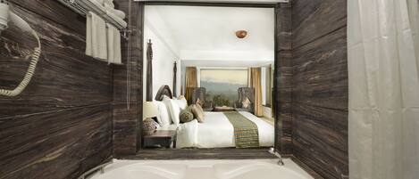 Un baño moderno con una bañera grande, paredes de madera y vistas a un dormitorio con cama y ventana.