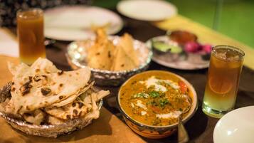 A table with a bowl of curry, naan bread, and a glass of iced tea.