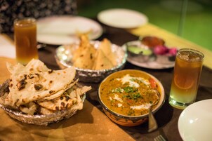 A table with a bowl of curry, naan bread, and a glass of iced tea.