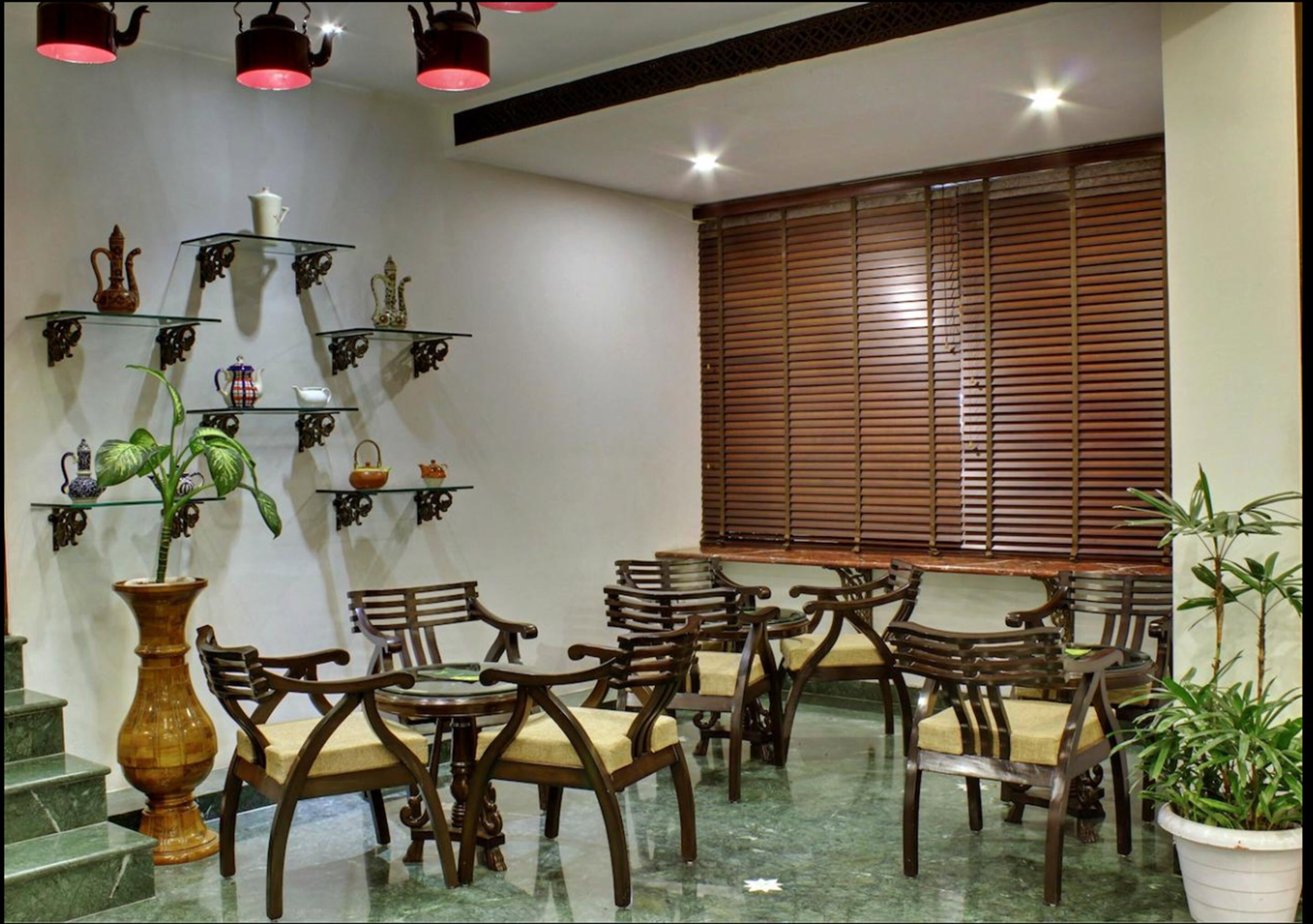 Un espace repas avec des chaises et des tables en bois, un escalier et un mur orné d’étagères où sont exposés divers objets.